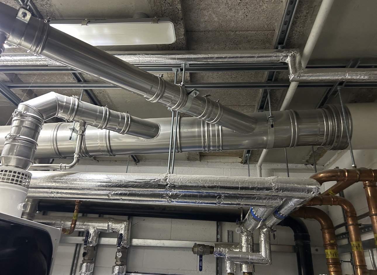 External stainless steel twin-wall commercial flue stack with branch connections on a UK commercial building