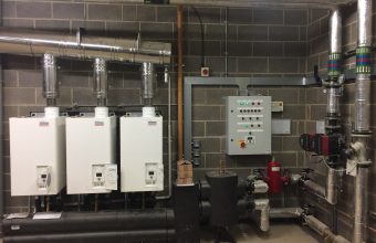 Rinnai Infinity continuous-flow gas water heater cascade installed in a London commercial plant room with stainless flue, low-loss header and circulation pump